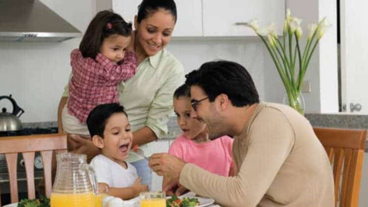 Family of two girls and a boy and couple. Man feeding boy.