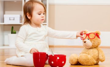 Toddler girl putting dress-up glasses on stuffed bear