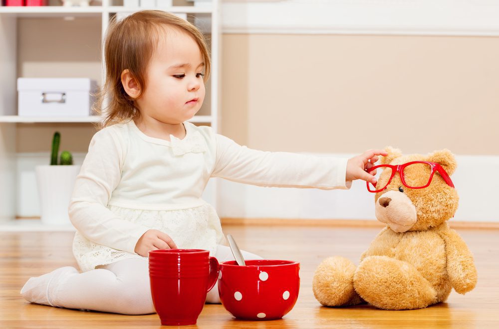 Toddler girl putting dress-up glasses on stuffed bear