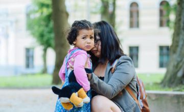 Mom holding fussy toddler who is crying, standing outdoors.