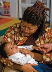 A child care educator holds and smiles at a baby.