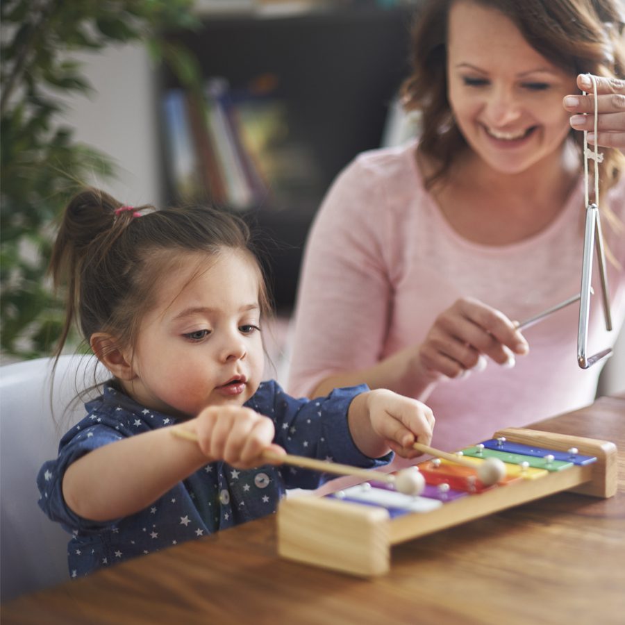 A young child plays on a toy xylophone while an adult looks on and plays the triangle.