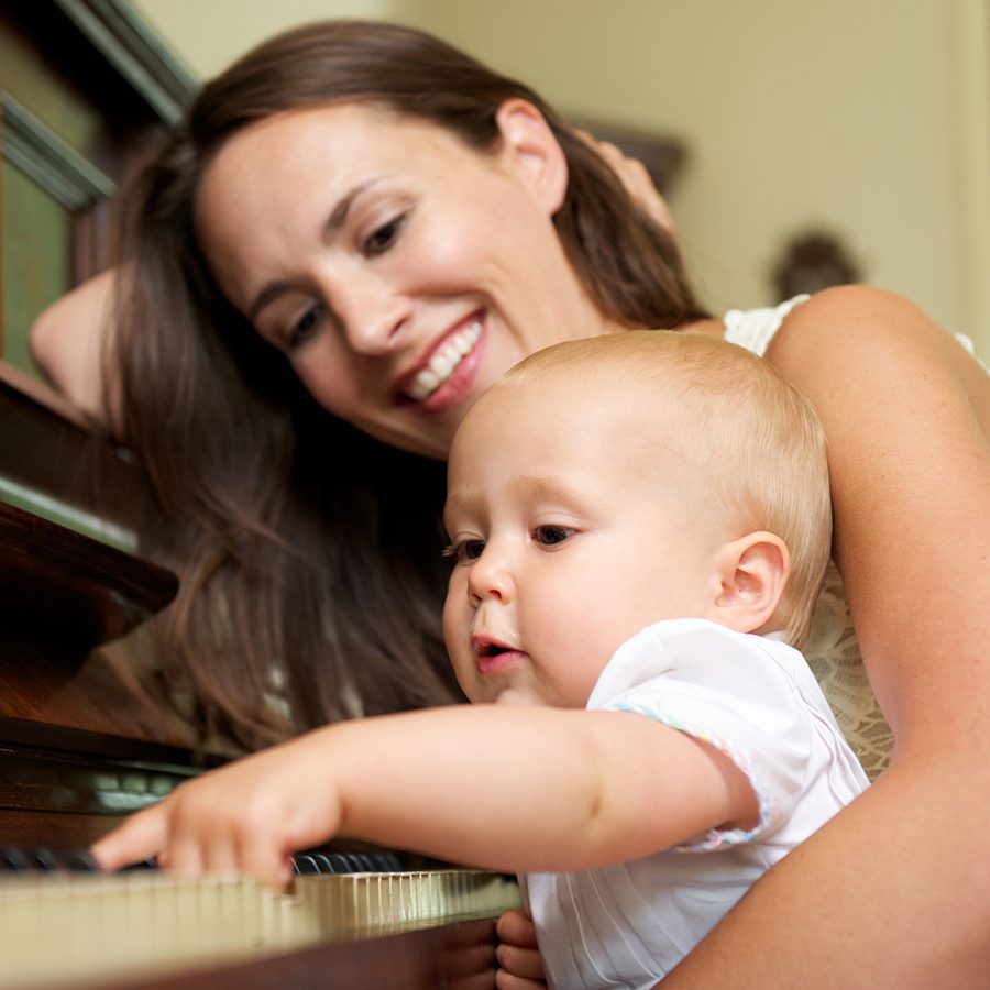 A baby plays the piano with their mother.