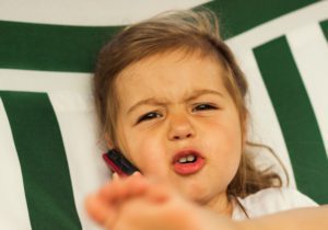 A toddler makes an upset face while holding a phone.