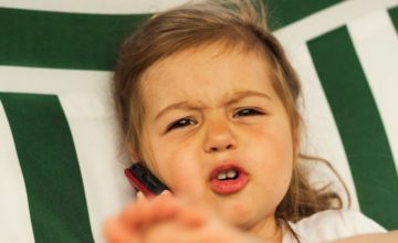 A toddler makes an upset face while holding a phone.