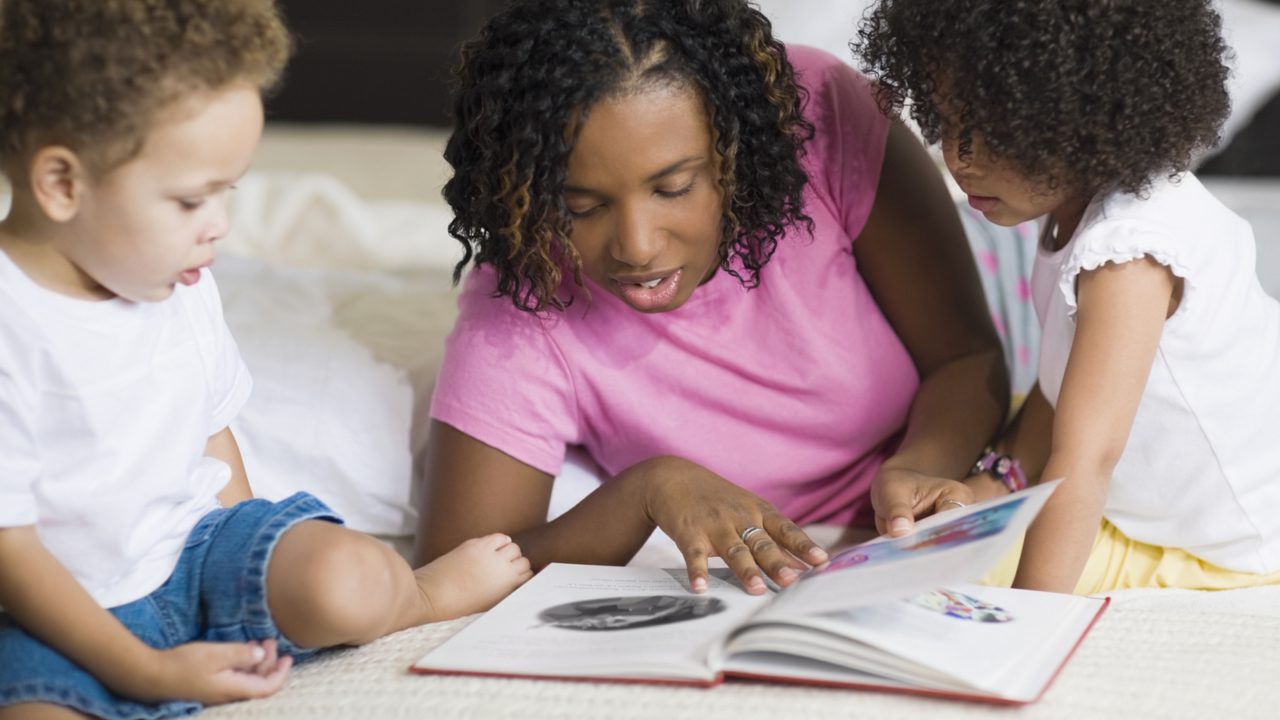 woman on bed reading with small girl and boy