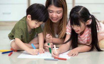 woman and two children around table coloring