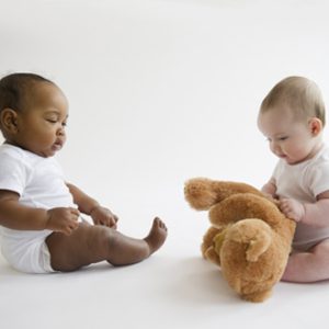 Two babies play with a teddy bear.