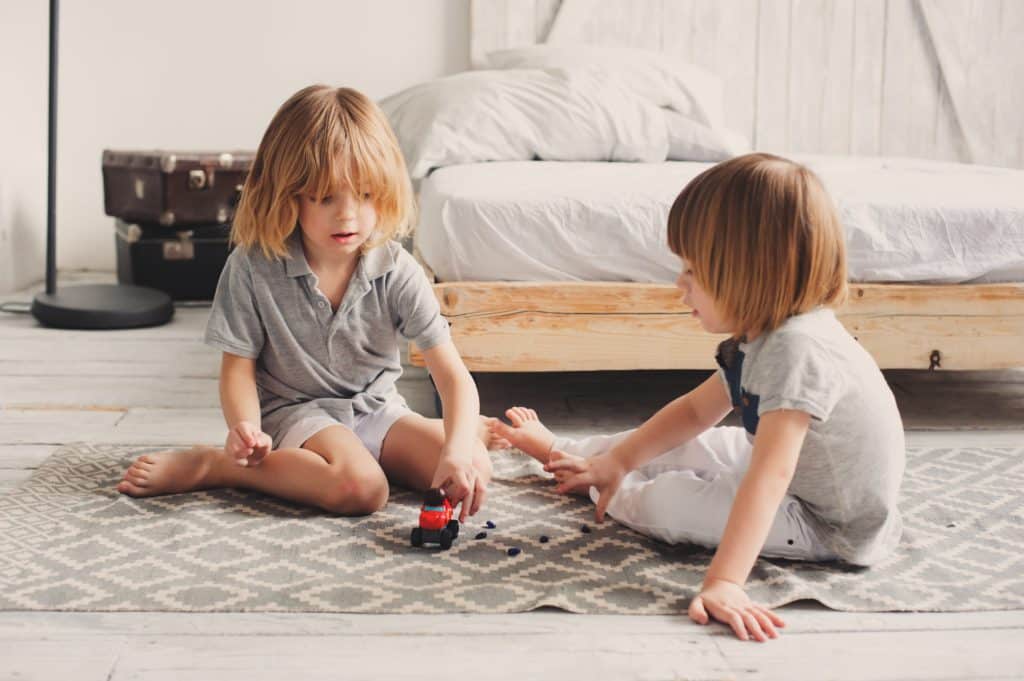 Two young children play with a toy car in a bedroom.