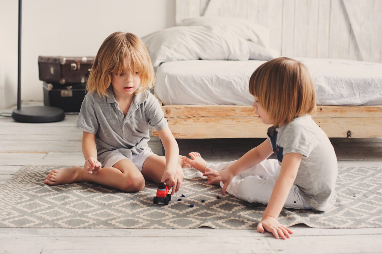 Two young children play with a toy car in a bedroom.
