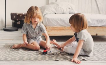 Two young children play with a toy car in a bedroom.