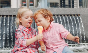 Two young children share a melting ice cream cone.