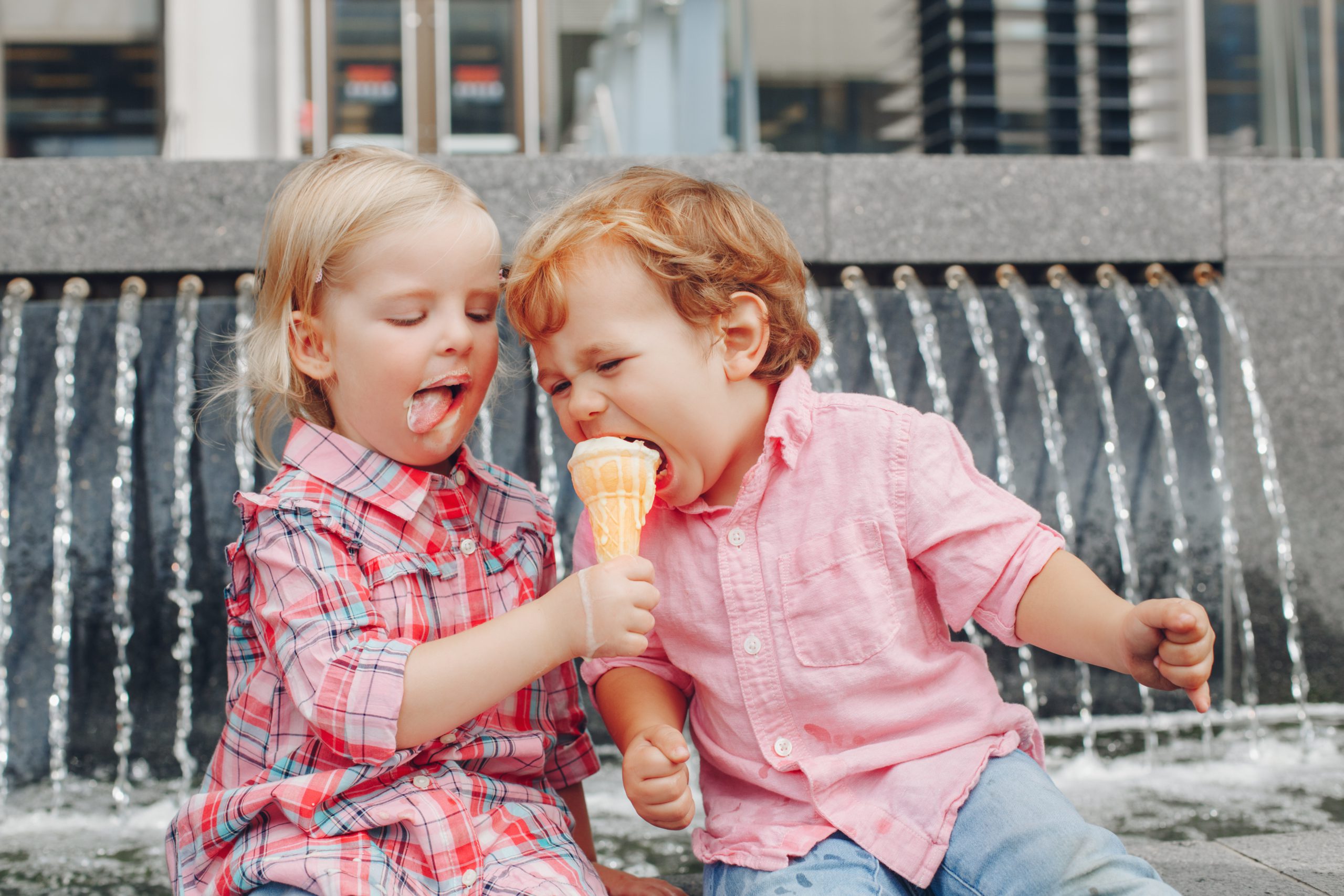 Two young children share a melting ice cream cone.