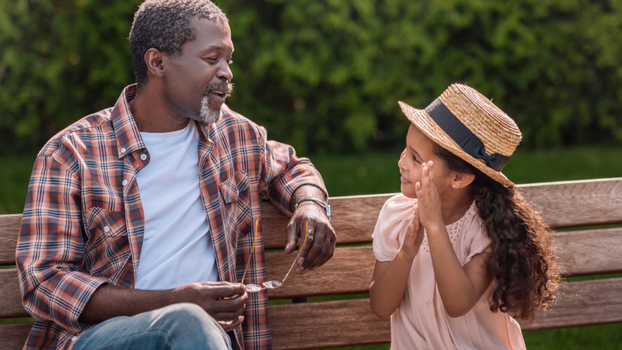 grandfather sitting on bench talking to grand-daughter