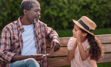 grandfather sitting on bench talking to grand-daughter