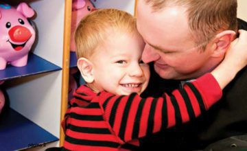 man holds young boy looking down at him while he smiles with big grin