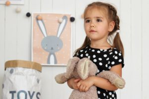 A young girl holds her toy bunny while looking at something in front of her.
