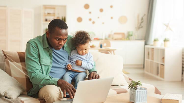 Parent holding a toddler and watching something on laptop