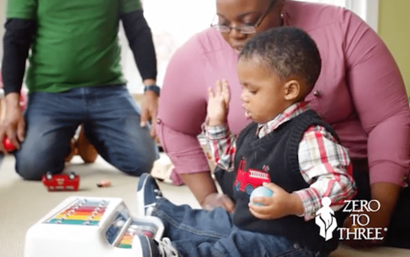 Early childhood educator watching toddler playing toy xylophone