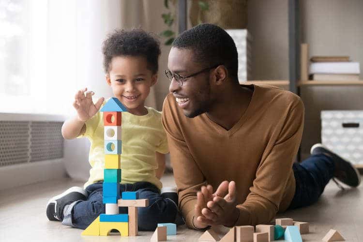 Young father laying on the floor with toddler playing with blocks