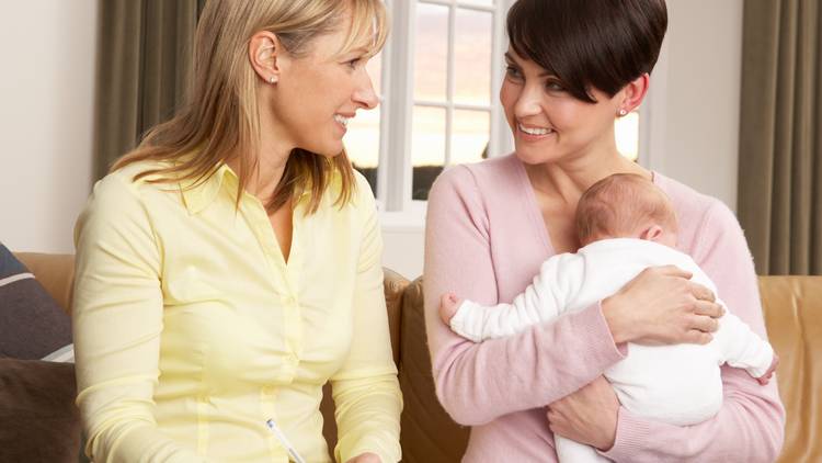 Mother with their baby smiling with home visiting professional