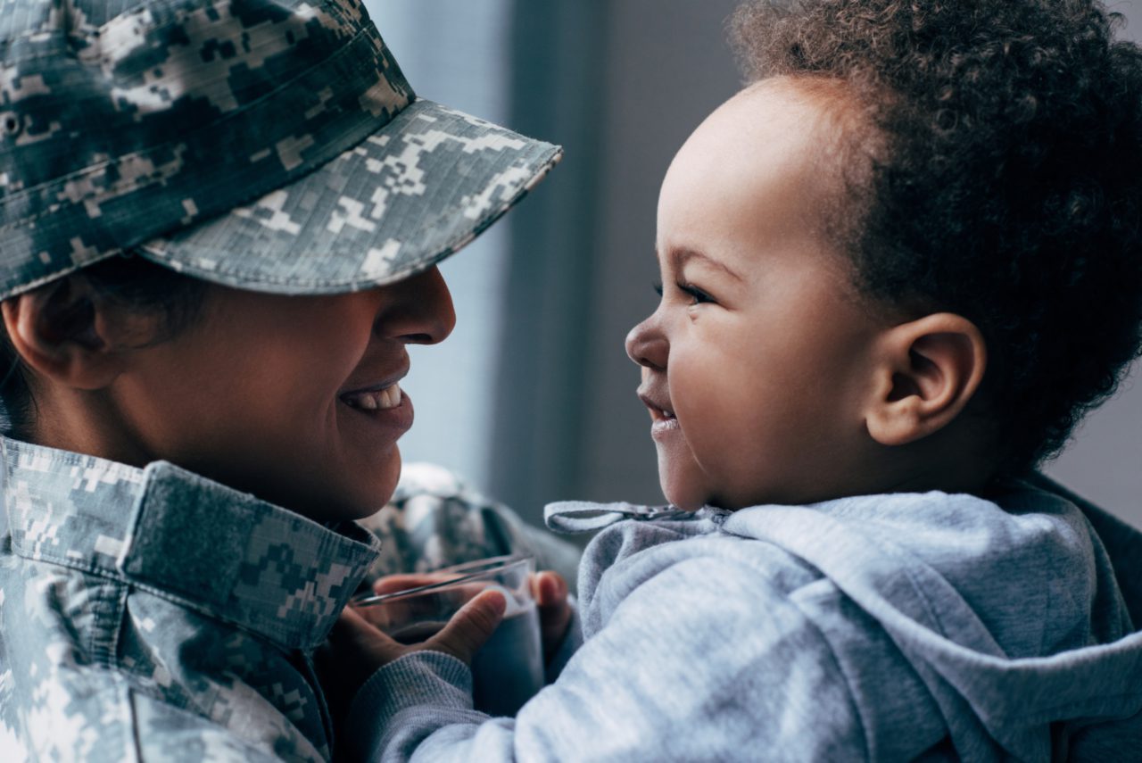 mother in military uniform holding toddler smiling at each other