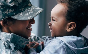 mother in military uniform holding toddler smiling at each other