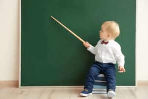 Toddler holding a pointer at a chalk board like a teacher