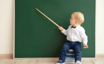 Toddler holding a pointer at a chalk board like a teacher