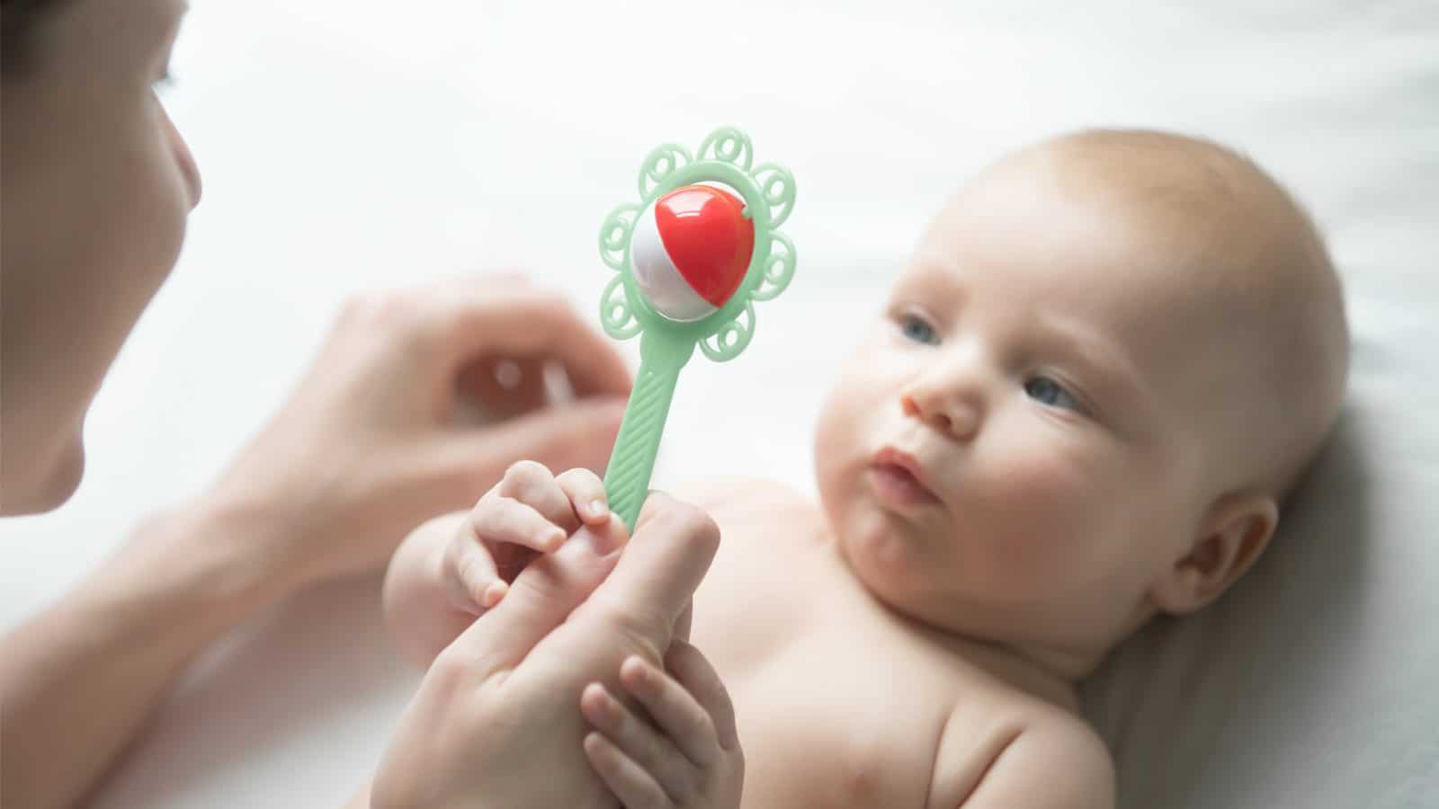 A baby looks at a rattle.