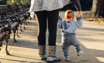 Mother holding toddler's hands as they walk