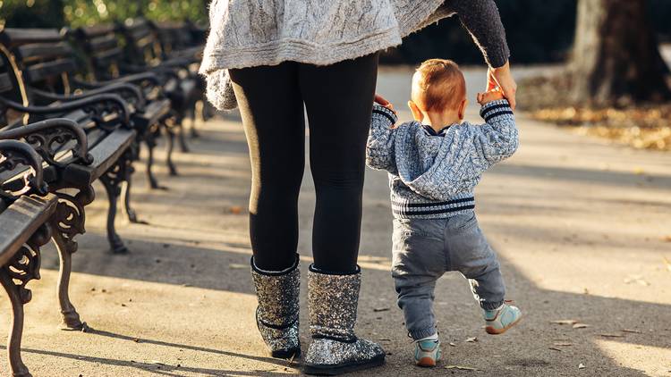 Mother holding toddler's hands as they walk