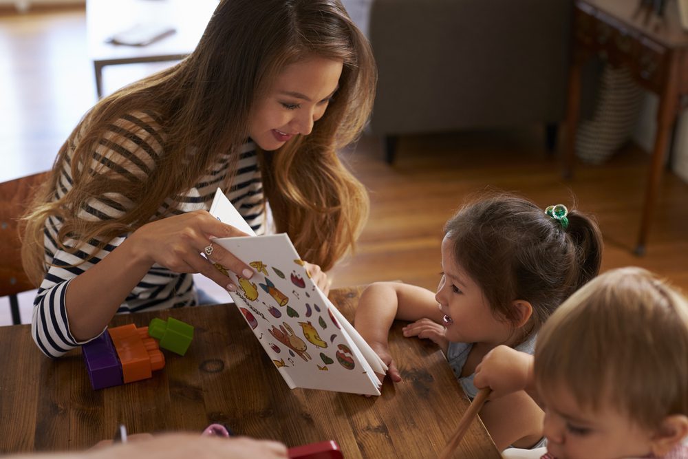Mother reading book with children at table