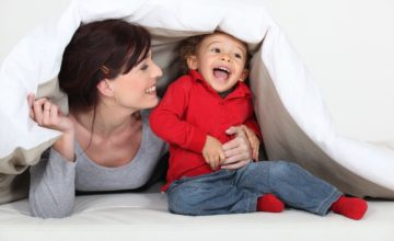 A mother and child play under a blanket.