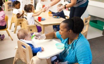 Child care teacher feeding infant in high chair