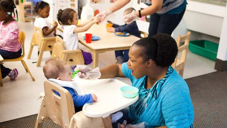 Child care teacher feeding infant in high chair