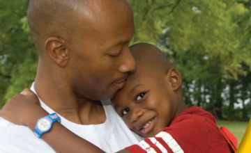 father holding son in arms looking down at him and child smiling at camera