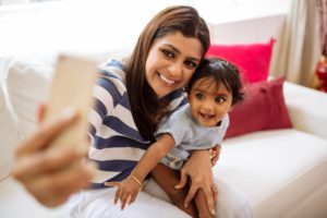 Mother holding toddler daughter on couch taking a picture together