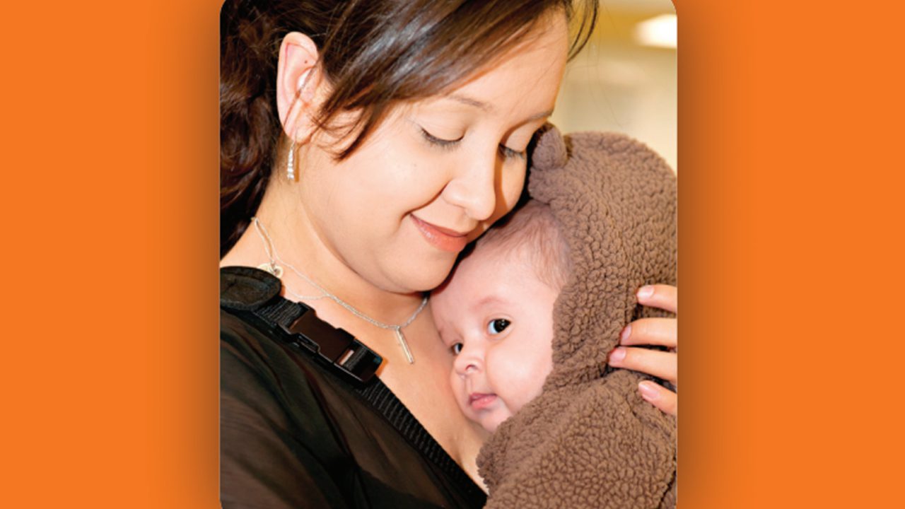 mother smiling holding baby in brown coat close to chest