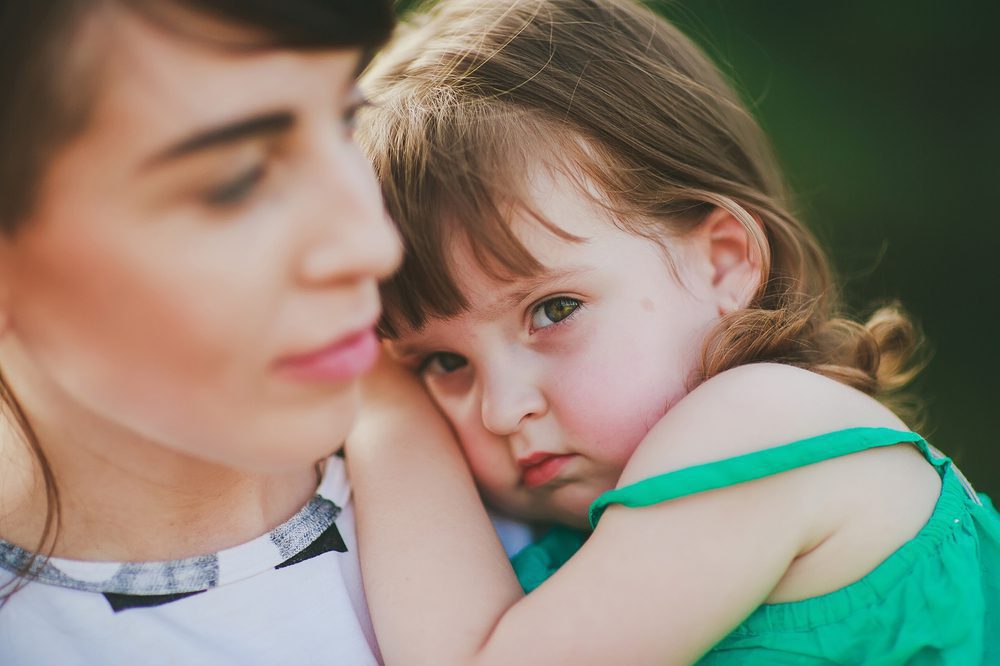 A child frowns as she is held by her mother.