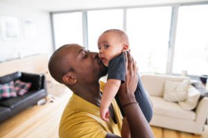 A father holds up and kisses his young baby.