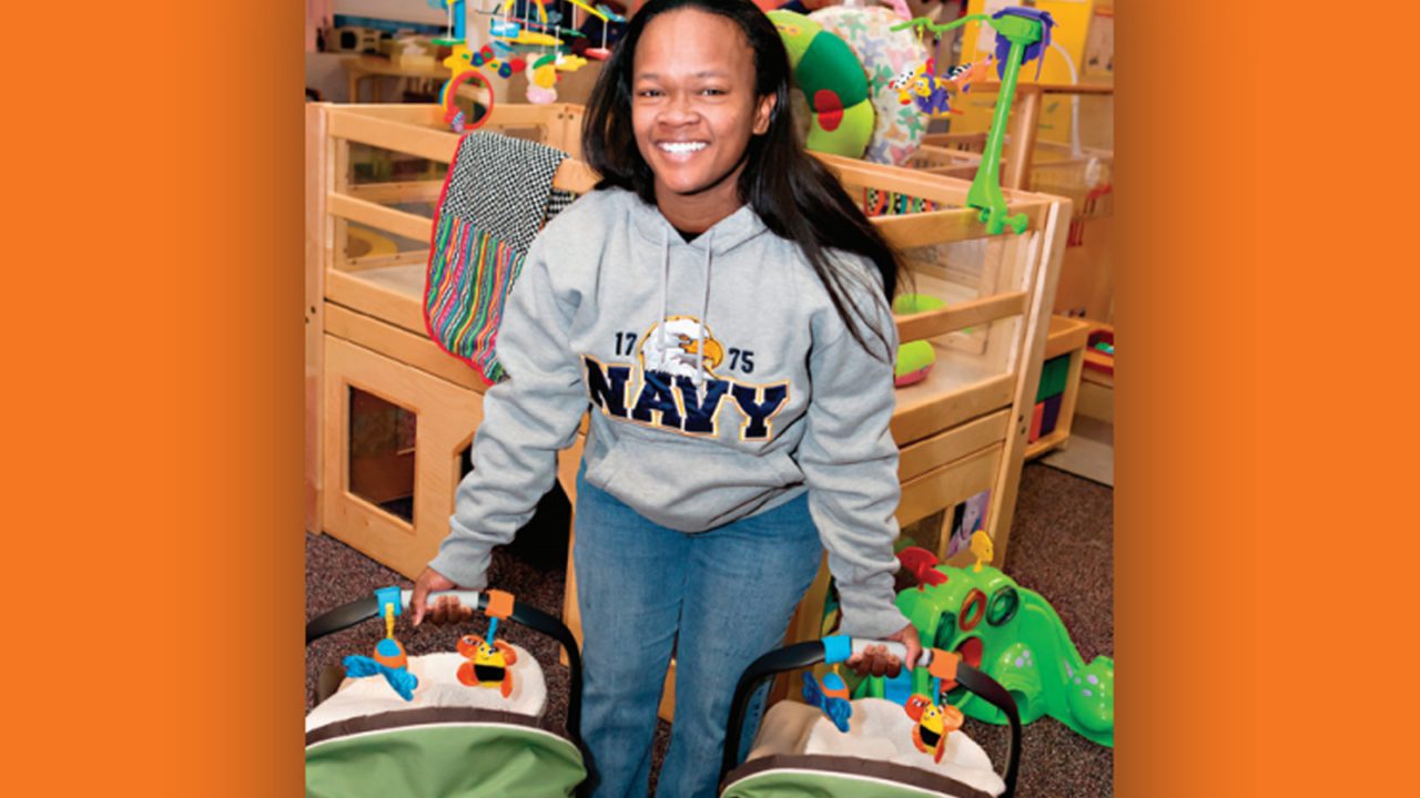 woman with Navy military sweatshirt holding two infants in car seat carriers