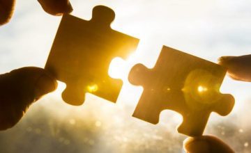 Hands holding puzzle pieces against a sunny background