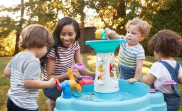 Adult with three toddlers playing with a toy for children outside