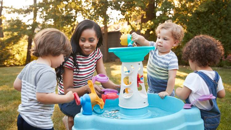 Adult with three toddlers playing with a toy for children outside