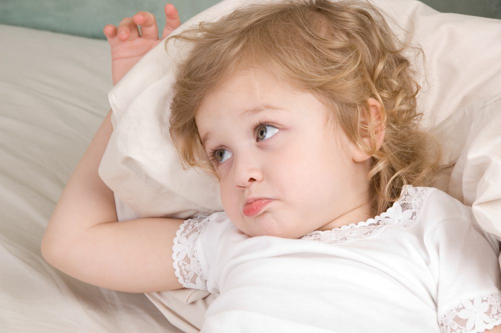 A young child lies in bed upset.