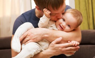 Man kissing infant he is carrying and cradling