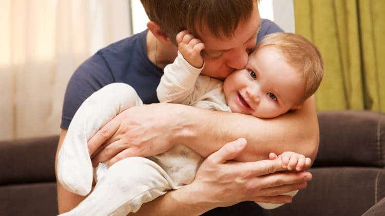 Man kissing infant he is carrying and cradling