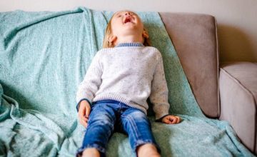 Child laying back on couch with mouth open