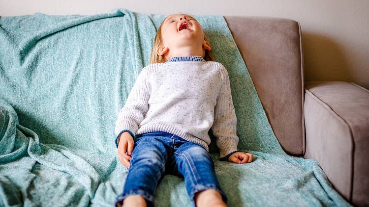 Child laying back on couch with mouth open